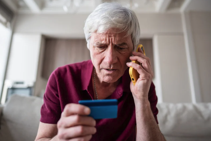 older man on the phone holding his credit card looking concered