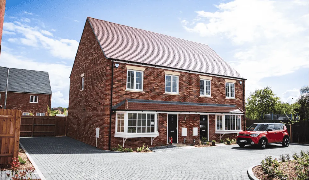 semi-detached new build red brick house with a large drive and a red car parked